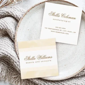 A product view of the front and back of a customizable square business card. The front has a soft cream watercolor effect on top and bottom borders. All text is gold-brown or sepia colored, a calligraphic script name above sans-serif title text in the clean white center. The back repeating the script name and title, with a centralized stack of phone, address, and website details below.