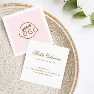 Front and back of a customizable square business card . The front features a delicate white frame around a light pastel pink panel with a custom logo. The back is pristine white with centered gold-brown calligraphy script for a name and clean sans-serif text stacked below with a professional title and contact details.