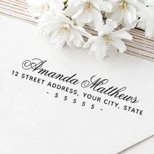 Custom self-inking stamp design featuring a flowing cursive script name above a single line of uppercase sans-serif address text and a spaced dashed ZIP code row.
