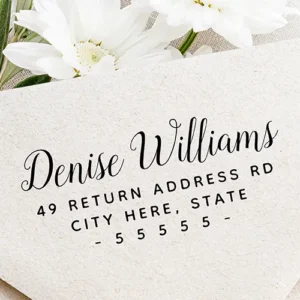 Rubber stamp design featuring a large sweeping cursive script custom name header above three lines of widely spaced uppercase sans-serif address typography flanked by hyphens.