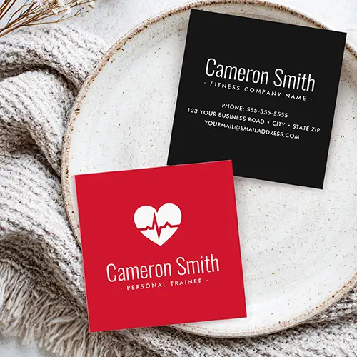 Double-sided square business card showing a vibrant red side with a white heart ECG pulse graphic and white headline text, beside a black reverse side displaying centered white contact text lines.
