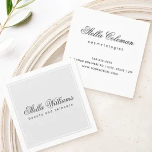 Double-sided square business card showing a light grey front panel with a double white frame and dark cursive script name, beside a crisp white reverse side displaying matching calligraphic name, profession title, phone number, address, and website URL.