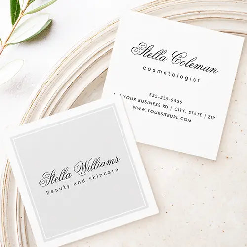 Double-sided square business card showing a light grey front panel with a double white frame and dark cursive script name, beside a crisp white reverse side displaying matching calligraphic name, profession title, phone number, address, and website URL.