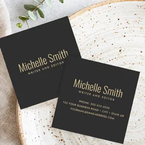 Square business card with a solid, very dark gray background. Centered on the card is the name printed in a warm yellow tone sans-serif font. Directly below the name is a smaller line of custom text in the same color, suggesting a job title or tagline.