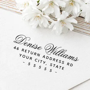 Custom self-inking stamp featuring a flowing cursive calligraphy script name above three lines of clean uppercase address text and a spaced dashed ZIP code line.