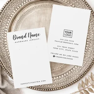 A white vertical earring display card featuring black cursive brand text at the top, website text at the bottom, and two subtle guide dots in the center.
