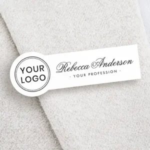 White rectangular plastic name tag featuring a left circular tab with space for a custom logo, alongside a custom name in flowing script calligraphy and a spaced sans-serif title line on the right.