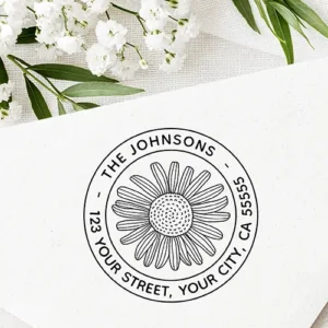 Circular rubber stamp design featuring a central line-art daisy flower enclosed in a double-ring frame with arched custom uppercase name and address text.