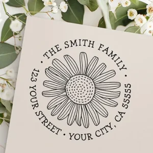 Circular rubber stamp featuring a hand-drawn daisy flower in the center surrounded by circular curved typewriter-style custom name and address text.