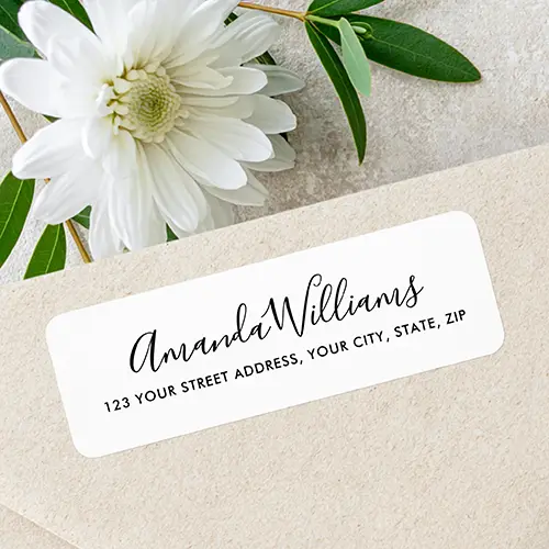 Horizontal rectangular white address sticker featuring black cursive script name text above a clean uppercase sans-serif street address line.