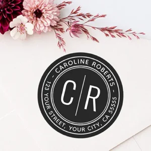 Round black self-adhesive sticker featuring white split initials separated by a vertical line, enclosed by double white border rings and curved return address text.