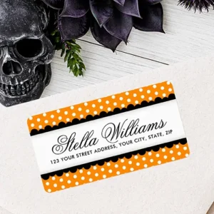 A rectangular address label featuring orange and white polka dot borders with black scalloped edges framing a central white banner displaying a name in cursive script and address details.