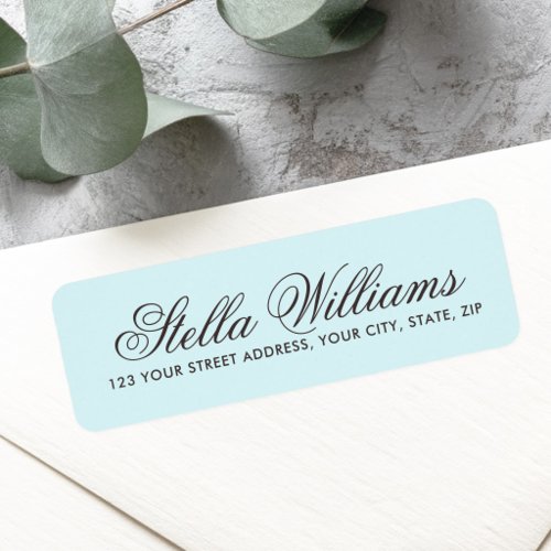 A rectangular return address label with rounded corners. The background is a soft light blue, featuring a large elegant script custom name and a clean sans-serif address below in dark ink.