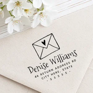 Rubber stamp design featuring an illustrated envelope with a heart motif, a playful handwritten script name, two lines of uppercase address text, and a dashed ZIP code row.