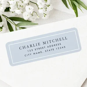 Rectangular address sticker featuring a soft dusty blue background framed by a white inner border with centered dark serif name and sans-serif address typography.