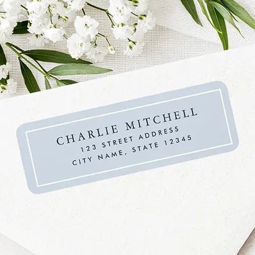 Rectangular address sticker featuring a soft dusty blue background framed by a white inner border with centered dark serif name and sans-serif address typography.