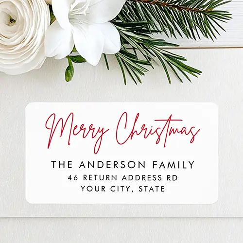 Horizontal rectangular return address label featuring a red script "Merry Christmas" greeting at the top, followed by a stacked black uppercase family name and two lines of street and city address text.