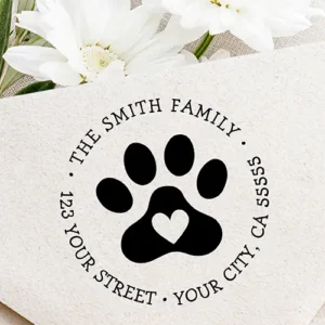 Circular return address stamp design featuring a solid pet paw with a center heart cutout, surrounded by arched uppercase custom name and address text in typewriter font.