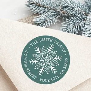 Round pine green return address sticker featuring a whimsical folk art style white snowflake illustration at the center, surrounded by curved uppercase serif text displaying a family name and complete address.
