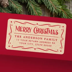 A rectangular self-adhesive return address label with printed light brown kraft paper background with rich red text and ornamental frame. The top displays a decorative "Merry Christmas" header with flourishing serifs, a horizontal divider, and three lines of custom family name and address text inside an ornate star-accented scroll border.