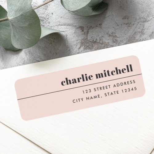 A rectangular return address label with rounded corners and a pale blush pink background. A black horizontal line separates the name in lowercase serif font from a right-aligned sans-serif address.