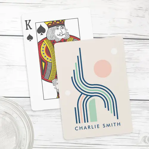 Personalized playing cards featuring retro abstract line art with curving stripes in navy blue, sage green, and pink, accented by circles and a half arch rectangle. Customizable name at the bottom.