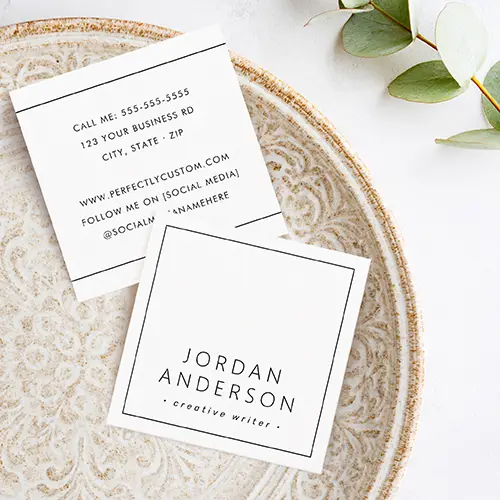 Two custom square business cards displaying front and back views. The front is a clean white square with a precise thin black square border framing centered name and title text in clean black fonts. The back is white with thin horizontal black lines near top and bottom, framing centered stacked blocks of contact and social media information in black. All fonts are clean sans-serif.