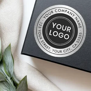 A circular return address label featuring a printed brushed silver look ring with company name and address text surrounding a central black circle with a logo placeholder