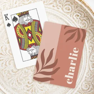 A rectangular custom playing card with rounded corners, featuring a vertically split background of dusty blush pink brown on the left and earthy terracotta on the right. Dark brown abstract leaf fronds decorate the opposite corners, and a custom name is written vertically on the right side in a thick, cream-colored serif font.