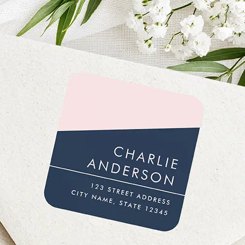 Square self-adhesive label split diagonally into blush pink and dark navy blue sections, featuring blush pink uppercase text for a name and right-aligned address lines.