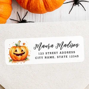 Horizontal white self-adhesive address label featuring a smiling watercolor pumpkin illustration with star accents next to black cursive name script and typewriter address text.