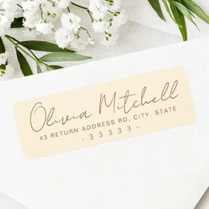 Horizontal warm cream self-adhesive label displaying warm brown hand-lettered cursive script for a name above clear, spaced sans-serif address details.