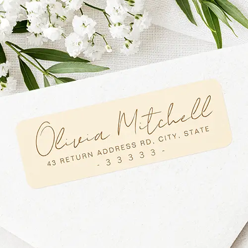 Horizontal warm cream self-adhesive label displaying warm brown hand-lettered cursive script for a name above clear, spaced sans-serif address details.