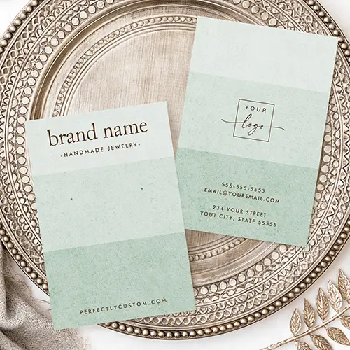 A vertical earring display card featuring three shades of pastel sage green with brown brand text at the top and two green guide dots in the center.