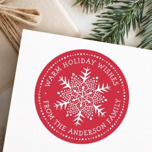 Round holiday sticker with red background, white folk art style snowflake, and customizable white family name and greeting. Perfect for sealing Christmas cards and gifts.