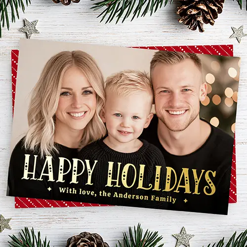 Horizontal full-bleed photo holiday card featuring gold Art Deco "Happy Holidays" text overlaid at the bottom, paired with a reverse side displaying diagonal white dotted stripes on a red background.
