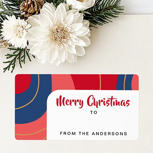 Rectangular sticker label featuring an abstract background of red, navy blue, and coral arches with golden-brown lines, enclosing a white text panel with red Merry Christmas script, a TO line, and a custom family sign-off at the bottom.