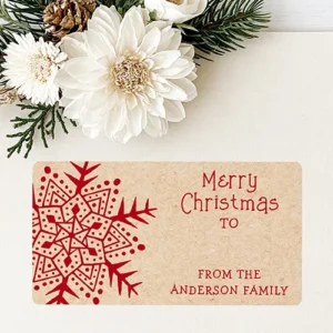 Rectangular sticker label with kraft paper background featuring a detailed dark red snowflake on the left, Merry Christmas typography with a TO line, and a custom family signature at the bottom right.