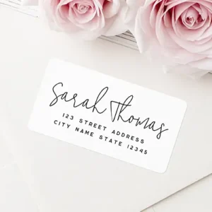 Rectangular address sticker featuring a white background with a black handwritten style cursive script name headline and centered block address typography below.