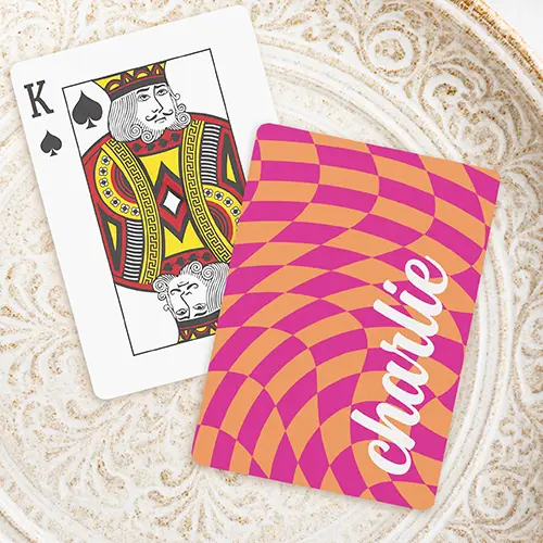 A playing card featuring a wavy, distorted psychedelic checkerboard pattern in alternating hot pink and bright orange squares. On the right side, a custom name is written vertically in a thick, flowing white script font.