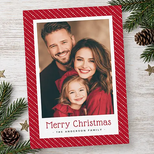 Vertical Christmas card featuring a red background with diagonal white dotted pinstripes framing a family picture in a white border with red Merry Christmas text below.