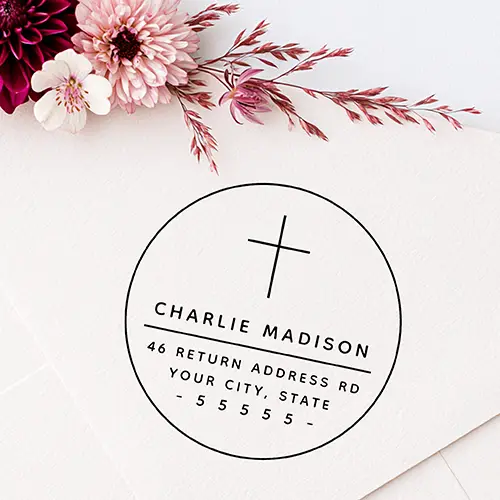 Modern minimalist circular rubber stamp design featuring a thin cross emblem at the top, a clean uppercase name, a horizontal divider line, two address lines, and a spaced ZIP code line framed with dashes.