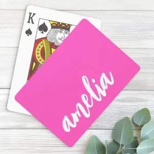Solid bright pink playing cards with your custom name rendered in a bold white calligraphic script font running vertically down the right-hand side.