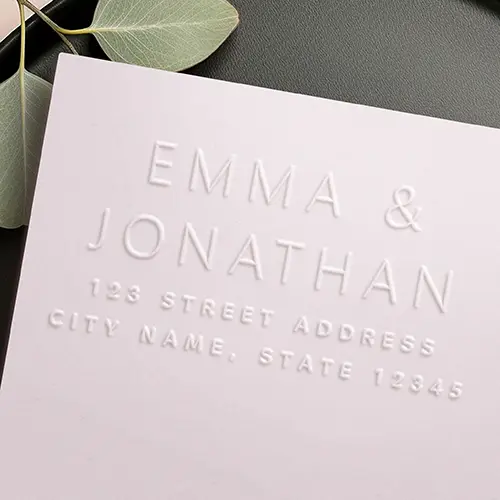 A 3D embossed impression on paper showcasing a centered four-line layout of clean, all-caps sans-serif lettering with a custom name block at the top and address details at the bottom.