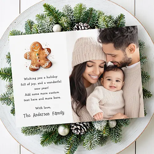 Horizontal holiday greeting card featuring a watercolor style gingerbread cookie illustration and custom text on the left side next to a large family photo portrait on the right side.