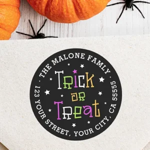 Circular black return address sticker featuring colorful, whimsical "Trick or Treat" text surrounded by white stars and curved white address typography along the outer rim.