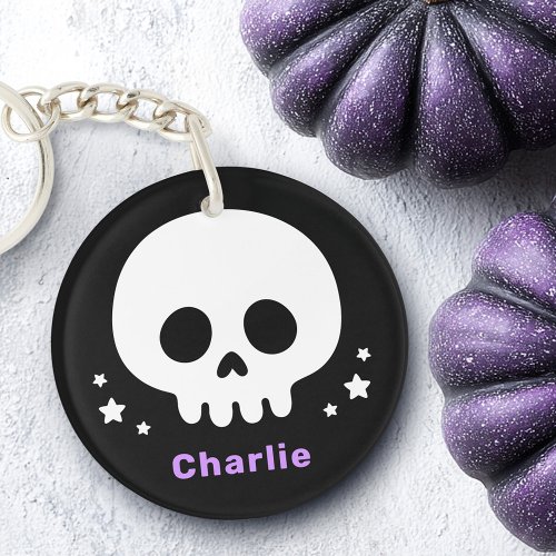 Personalized Halloween skull keychain featuring a white cartoon skull, white stars, and custom lavender text on a bold black background.