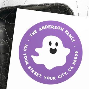 Round Halloween return address label with purple background, smiling white ghost in the center, and family name and address in white bold letters around the border. Fun, family-friendly design.