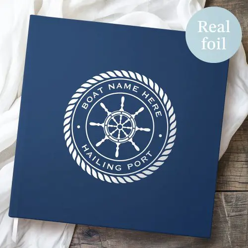 A deep navy blue hardcover guest book with custom real foil (silver, gold, or rose gold) featuring a ship's wheel emblem, boat name, and hailing port text.