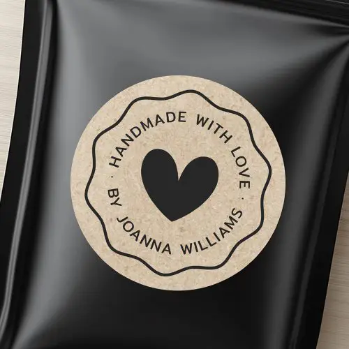 A round sticker with a printed kraft paper texture, a black heart in the center, a scalloped border, and customizable text saying "Handmade with Love".